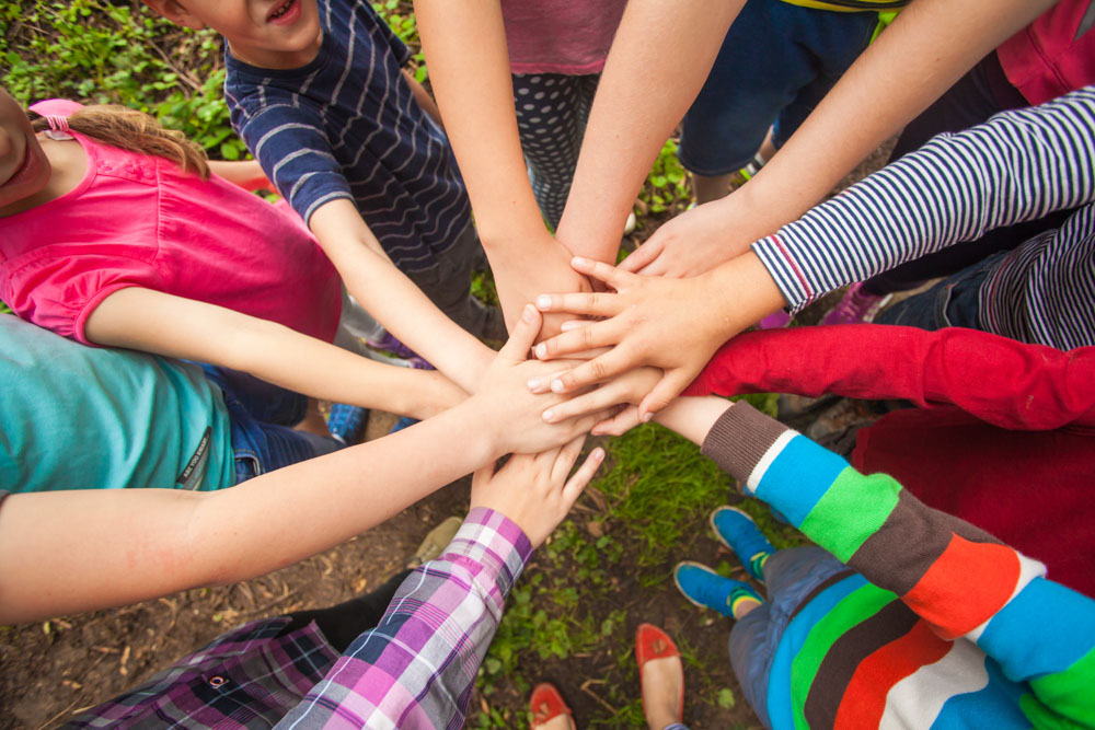 Das Bild zeigt eine Gruppe von Kindern, die im Kreis stehen und die Hände aufeinander legen.