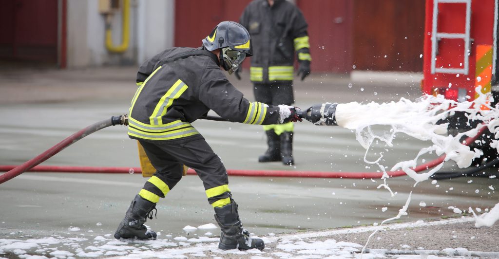 Das Bild zeigt einen Feuerwehrmann, der einen Schlauch in der Hand hält.